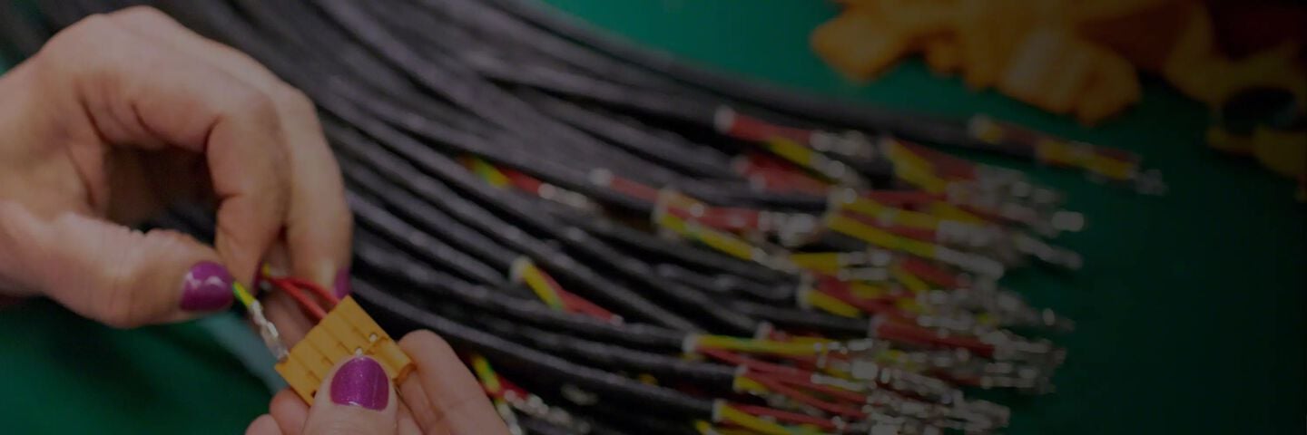 Een afbeelding van een hand die elektrische draden verbindt met een gele hub, met een stapel extra draden op de achtergrond.